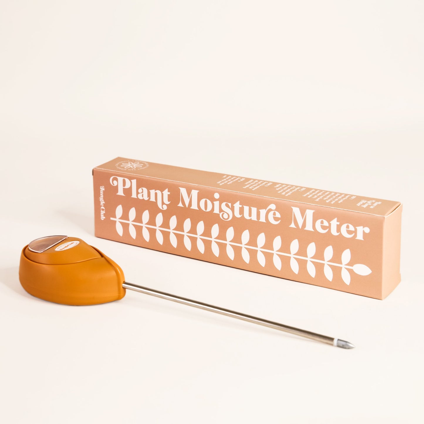 Orange moisture meter laying besides packaging that reads 'plant moisture meter' along the side of white leafy design. The moisture meter has an upside down teardrop shape and metal probe running from base. 