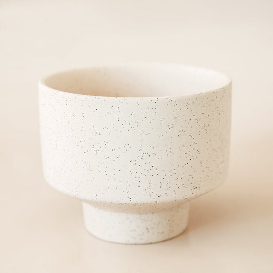 Ivory cylinder pot that tapers into a smaller base. The pot is covered in black speckles.