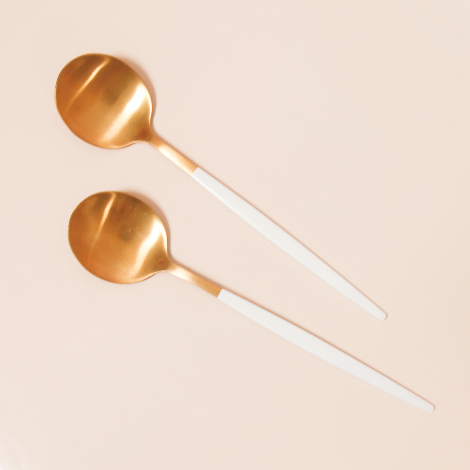 On a cream background is two brass planting spoons with a white handle that has a pointed end.