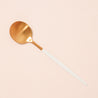 On a cream background is a brass planting spoons with a white handle that has a pointed end.
