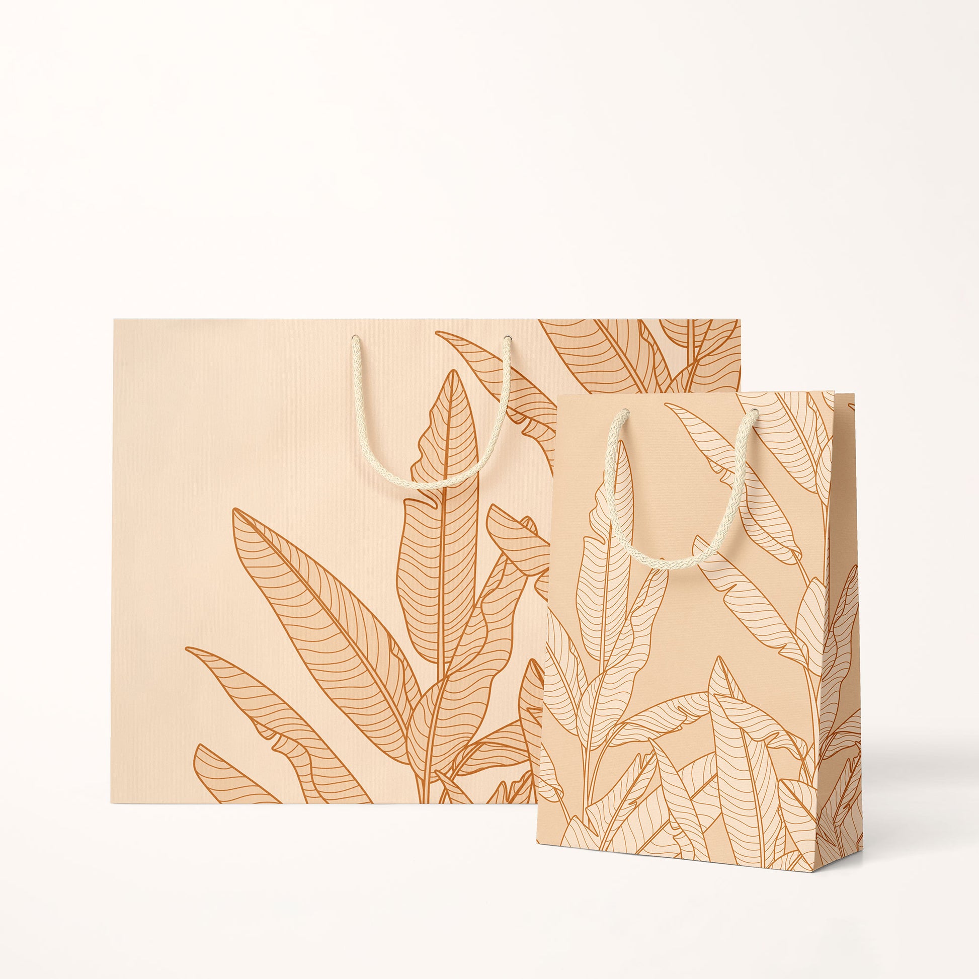 Two sizes of paper gift bags with a cream cotton handles and super light shade of salmon pink with graphics of banana leaves.
