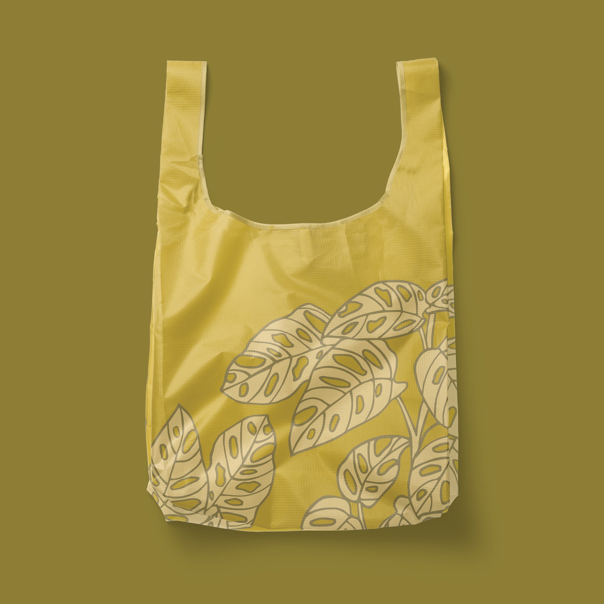 Photographed in front of a green background is a green nylon reusable bag with a lighter green Swiss cheese plant print on the front and back.
